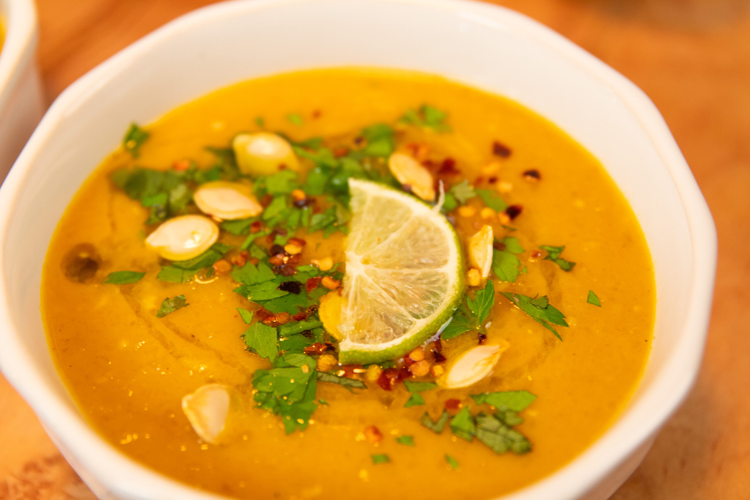 Pumpkin Coconut Soup in a white bowl with cilantro, lime and pumpkin seeds as garnish