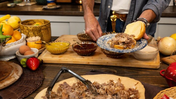 A photo of Trace about to add shredded BBQ pork onto a hamburger bun.